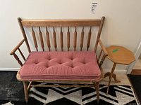 Solid wood vintage bench with pink tufted cushion and wood octagonal plant stand next to it, sitting on a black and white patterned rug.