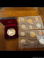 Two sets of 1991 Canadian uncirculated coins in original sealed cellophane wrappers alongside a silver dollar commemorating Vancouver in a protective display case.