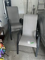 Four matching patio chairs stacked and arranged in garage beside parked vehicle. Chairs show black metal frame and grey fabric seats.