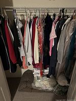 Full view of ladies clothing hanging on a closet rod with cushions and soft items on the floor beneath