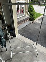 Full view of white metal clothing rack showing the front and top horizontal hanging bar with base for support.