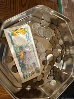 Photo of mixed Canadian and foreign coins in a metal container along with a folded Bahamas one dollar bill showing marine and flower designs.