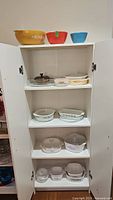 Wide view of cabinet shelf with the mixing bowls on top shelf and various CorningWare casseroles and lids on shelves below