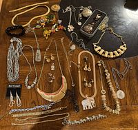 Full view of all costume jewelry items including necklaces, earrings, bracelets, and two pocket watches displayed on wooden table.