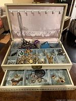 Jewelry box open displaying multiple compartments filled with various costume jewelry items including necklaces, brooches, and earrings.