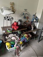 Wide shot of various garden decor items arranged on and under two-tier shelving including crane statues, metal cat figure, colorful windmill, red flower pots, and small animal statues.