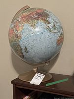 Full view of the globe showing continents and oceans on a beige plastic stand with a MaxSold tag.