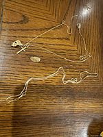 Fine cable chain with cross and second charm alongside intact rope chain and shield-shaped pin displayed on wood surface