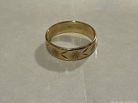 Front-facing view of gold band ring showing engraved starburst and arrow pattern.