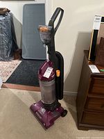 Full front view of purple Hoover WindTunnel upright vacuum cleaner showing handle, dustbin, hose and base unit with dial and wheels.
