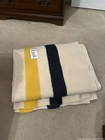 Folded blanket on carpet showing cream base and navy and yellow stripes.