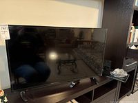 Front view of the Insignia 39 inch flat screen TV on a dark wood stand with remote in front.