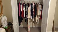 Photo showing a collection of women's clothing hung inside a closet including dresses and pant suits in various colors and patterns.