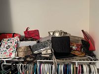 Wide view showing overall lot of assorted ladies purses, clutches, and wallets in various colors and styles arranged on a shelf.