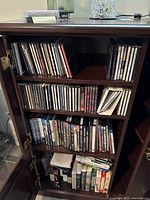 Full wooden cabinet with shelves containing CDs, DVDs, and VHS showing the quantity and storage method