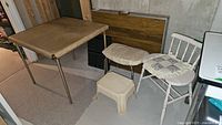 Set of folding table, wooden stools and chair with cushions, and plastic step stool visible in basement setting.
