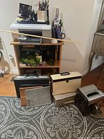 Image showing wooden office cart with multiple shelves filled with office supplies, briefcases in front, and paper shredder to the side