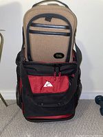Photo showing the two camera bags stacked, large black and red bag on bottom and smaller tan and black bag on top