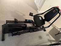 Side view showing padded seat, backrest, and pedals with adjustable straps.