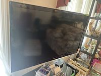 Front view of Samsung 46 inch TV showing screen and attached stand, placed indoors near window and shelving.