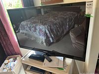 Samsung 46-inch Plasma TV shown turned off inside a room with bed and furniture reflected.