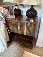 Front and top of one side table showing wood grain veneer, drawer closed, with lamp and acrylic decor on top.