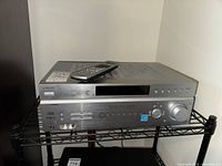 Front view of the Sony STR-K870P receiver with remote on top, showing buttons, volume knob, and front input/output ports.