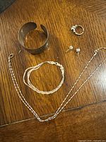 Overview photo showing all items together: chain necklace, braid style bracelet, cuff bangle, ring and earrings on wood table