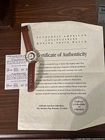 Watch with brown leather strap resting on Certificate of Authenticity paperwork from Authentic American Collectibles.