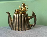 Front view of silver-plate teapot trinket box showing gold-tone tea set on lid