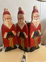 Front view of three hinged wooden Santas standing upright