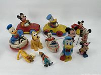 Overview of all 12 vintage Disney toys featuring Mickey Mouse, Donald Duck, Pluto, Goofy, and Minnie Mouse including several small vehicles and figurines.