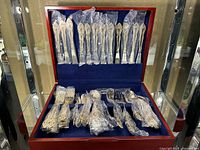 Full set of gold plated silverware in display case with pieces wrapped in protective plastic.