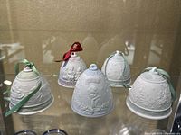 Five assorted Lladro porcelain bells displayed together, showing different embossed designs and ribbon colors.