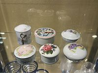 Top view of six small lidded porcelain containers, showing floral and bird designs on lids and sides.