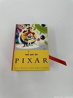 Yellow cover box with Pixar characters printed and title 'The Art of Pixar 100 Collectible Postcards'