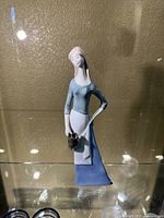 Front view of the German porcelain figurine showing the woman in a blue dress holding a black pitcher.
