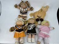 Group photo showing four Cabbage Patch dolls in cheer uniforms and one in pink outfit along with a plush horse