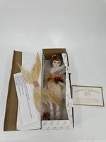 Full view of porcelain doll in cardboard box with certificate of authenticity included.