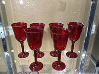 Six red stemmed glasses shown grouped on a shelf with reflective background