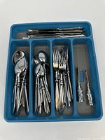 Overview of the blue flatware tray containing Coca-Cola branded forks, knives, and spoons, and two butter spreaders on the right side.