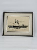 Full view of the framed black and white print depicting two tall ships sailing with a distant shoreline and seagull overhead, mounted behind glass in a silver and black frame.