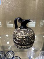 Front and side views of the small ceramic pitcher featuring black and red ancient Greek/Museo style decorative motifs and figures