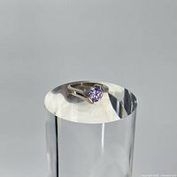 Sterling silver ring with round amethyst stone on a reflective cylindrical stand.