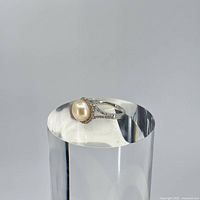 Sterling silver ring displayed on a reflective surface showing the pearl and rhinestone details.