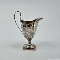 Full side view of the sterling silver cream jug showing the engraved detailing, handle, and pedestal base.