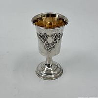 Front and side view of sterling silver goblet cup with embossed decorative pattern and gold-tone interior.