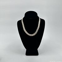 The sterling silver braided necklace displayed on a black bust stand showing the full necklace length and design.