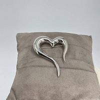 Sterling silver open heart-shaped pin resting on a gray cushion for display, showing its smooth polished surface and distinct shape.