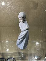 Front view of the Zaphiv porcelain figurine of a young girl in a flowing dress with arms crossed.